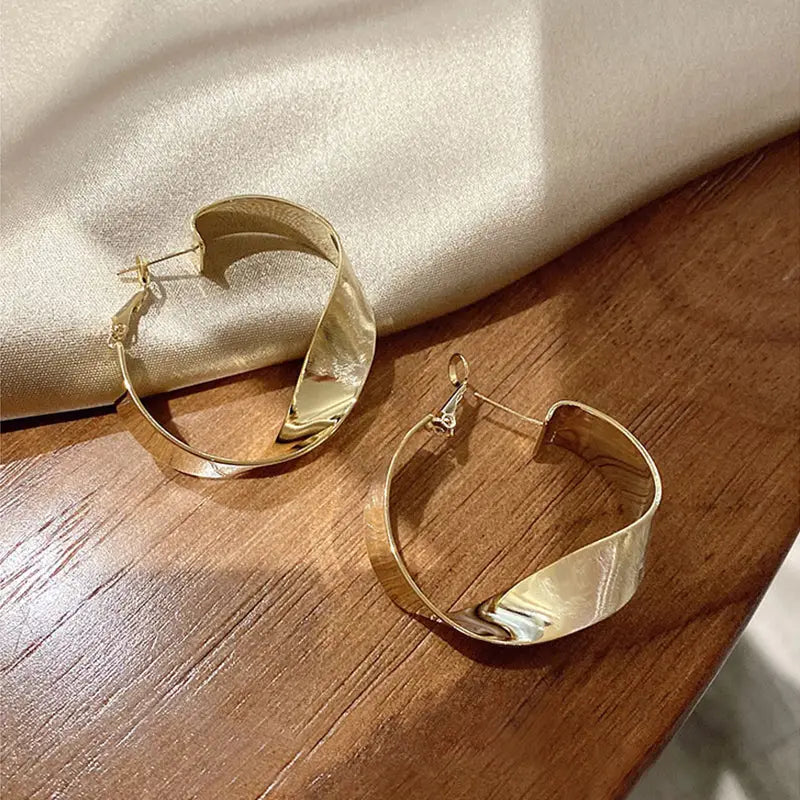 Grande boucle d'oreille dorée en forme de créole élégante sur une surface en bois et en tissu satiné.