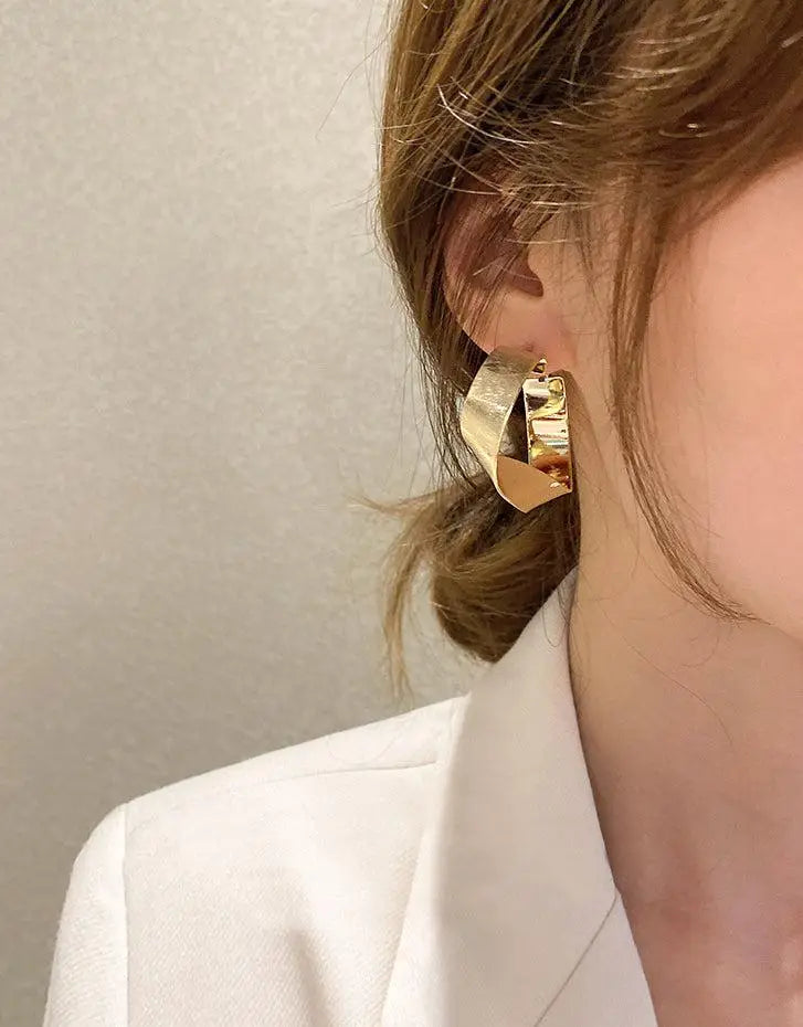 créoles dorées élégantes portées par une femme avec une coiffure chignon, fond clair