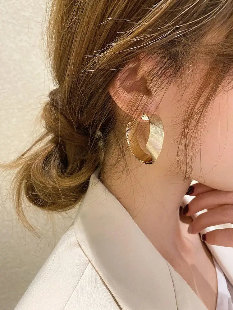 boucles d'oreilles créoles dorées en métal portées par une femme avec une coiffure décontractée et un blazer beige