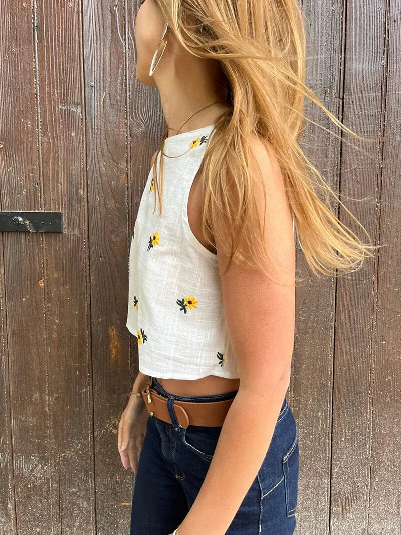 top blanc fleuri sans manches misha porté avec jean, parfait pour un look estival et élégant avec des motifs floraux jaunes