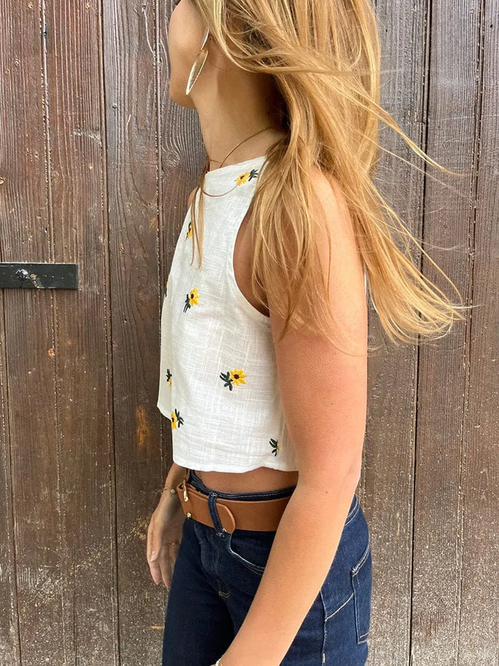 top blanc fleuri sans manches misha porté avec jean, parfait pour un look estival et élégant avec des motifs floraux jaunes
