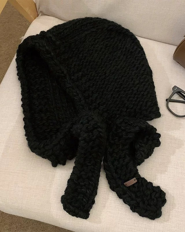 Écharpe cagoule en grosse maille noire élégante posée sur un canapé, idéale pour la mode hivernale et le style.