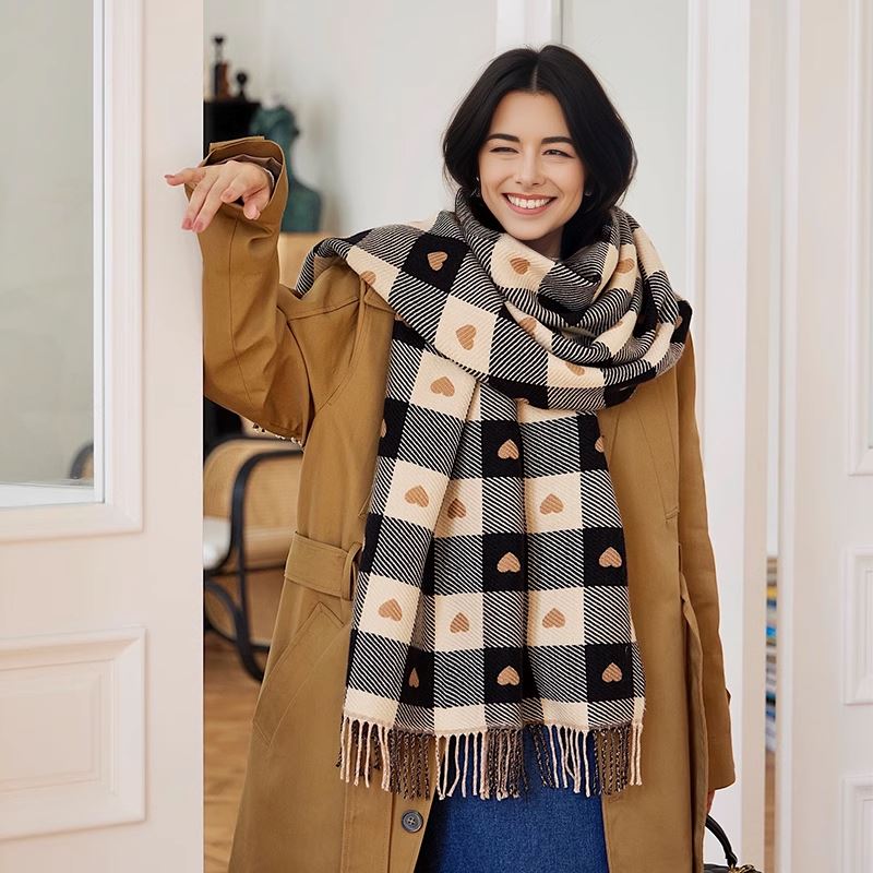 femme portant une écharpe en laine et cachemire avec motifs de cœurs, vêtue d'un manteau beige, et souriante en intérieur