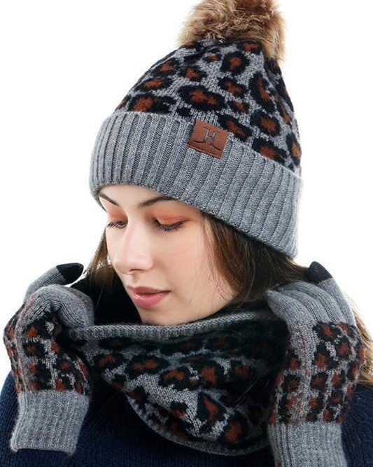 Femme portant l'ensemble bonnet, écharpe et gants Gina en tricot gris avec motif léopard pour l'hiver.