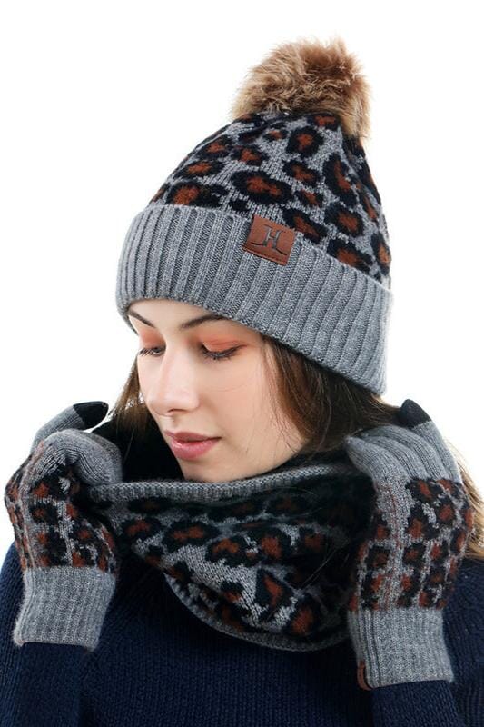 Femme portant l'ensemble bonnet, écharpe et gants Gina en tricot gris avec motif léopard pour l'hiver.