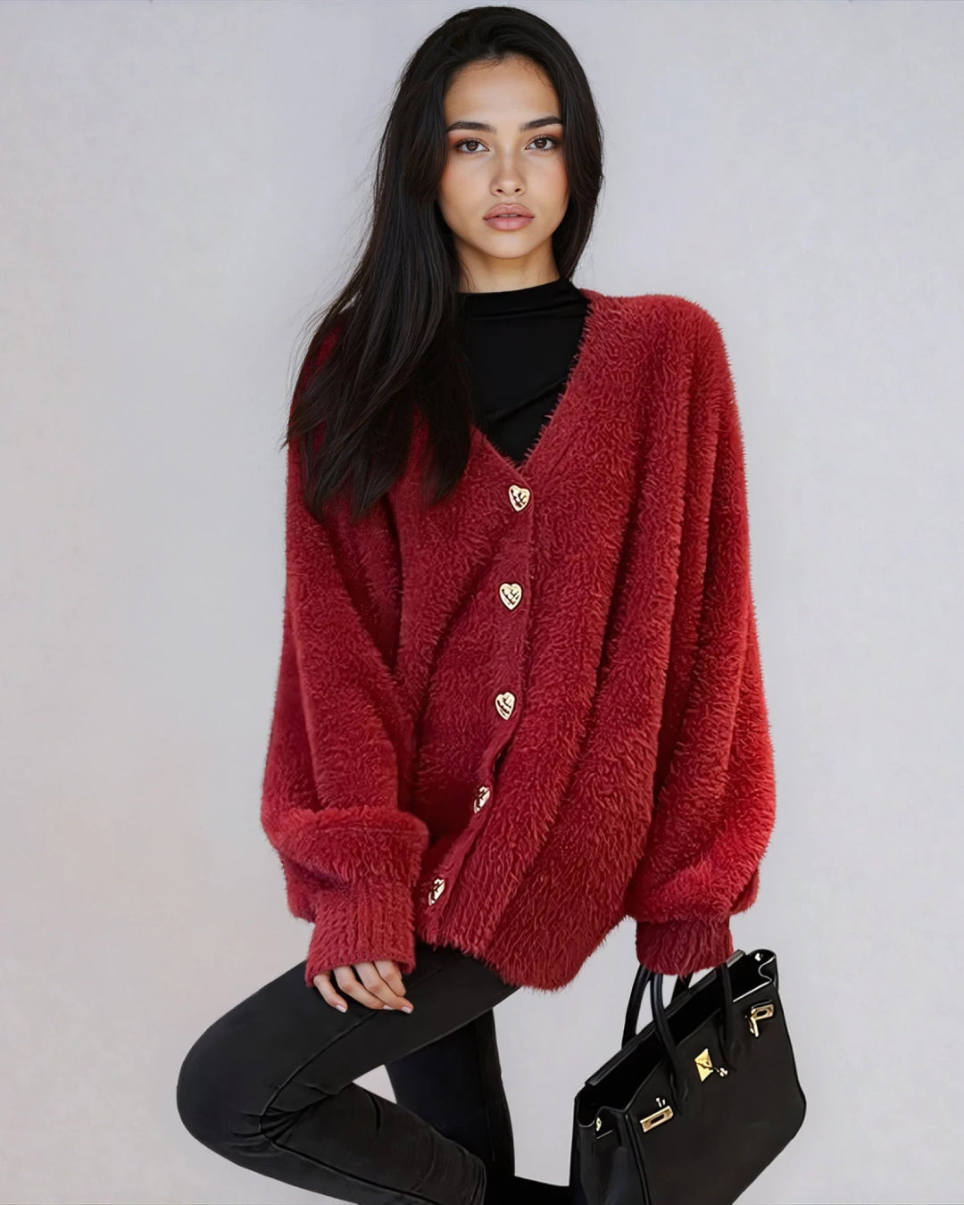 Femme portant un gilet rouge oversize en matière fluffy avec boutons en forme de cœur, tenant un sac noir élégant.