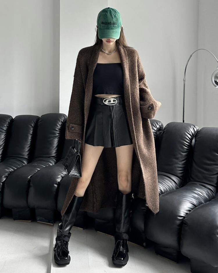 Femme portant un gilet long en grosse maille marron Thaïs, avec un look tendance urbain, casquette verte et bottes noires.