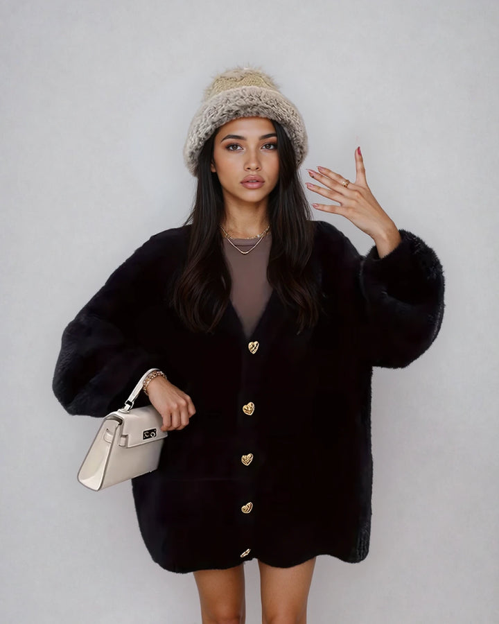Leïla porte un gilet oversize fluffy noir avec boutons dorés, accessoirisé d'un chapeau en laine et un sac à main beige.