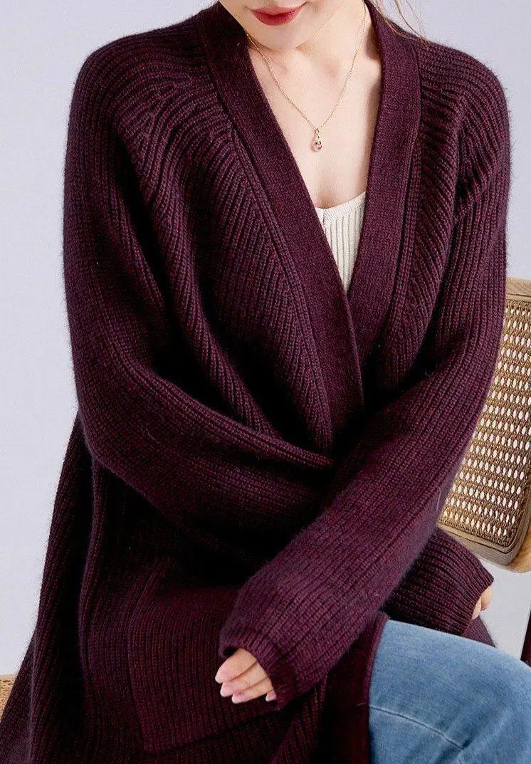 Femme portant un gilet long en laine et cachemire couleur bordeaux, assise sur une chaise, tenue décontractée et élégante.