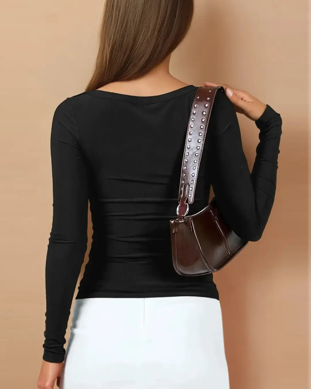 femme portant un t-shirt manches longues rose moulant, vu de dos, avec une jupe blanche et un sac marron élégant