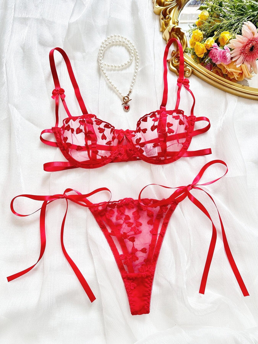 ensemble de lingerie sexy rouge transparent avec des motifs floraux, présenté avec un collier de perles et un miroir doré