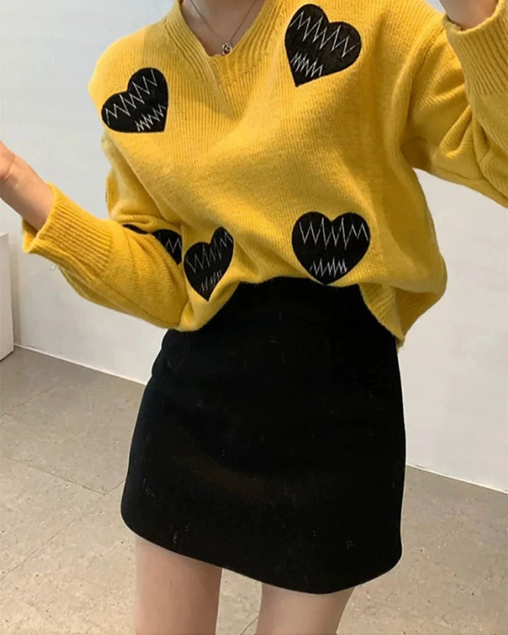 Modèle portant une jupe courte avec doublure short Nellie, combinée à un pull jaune à motifs cœur.