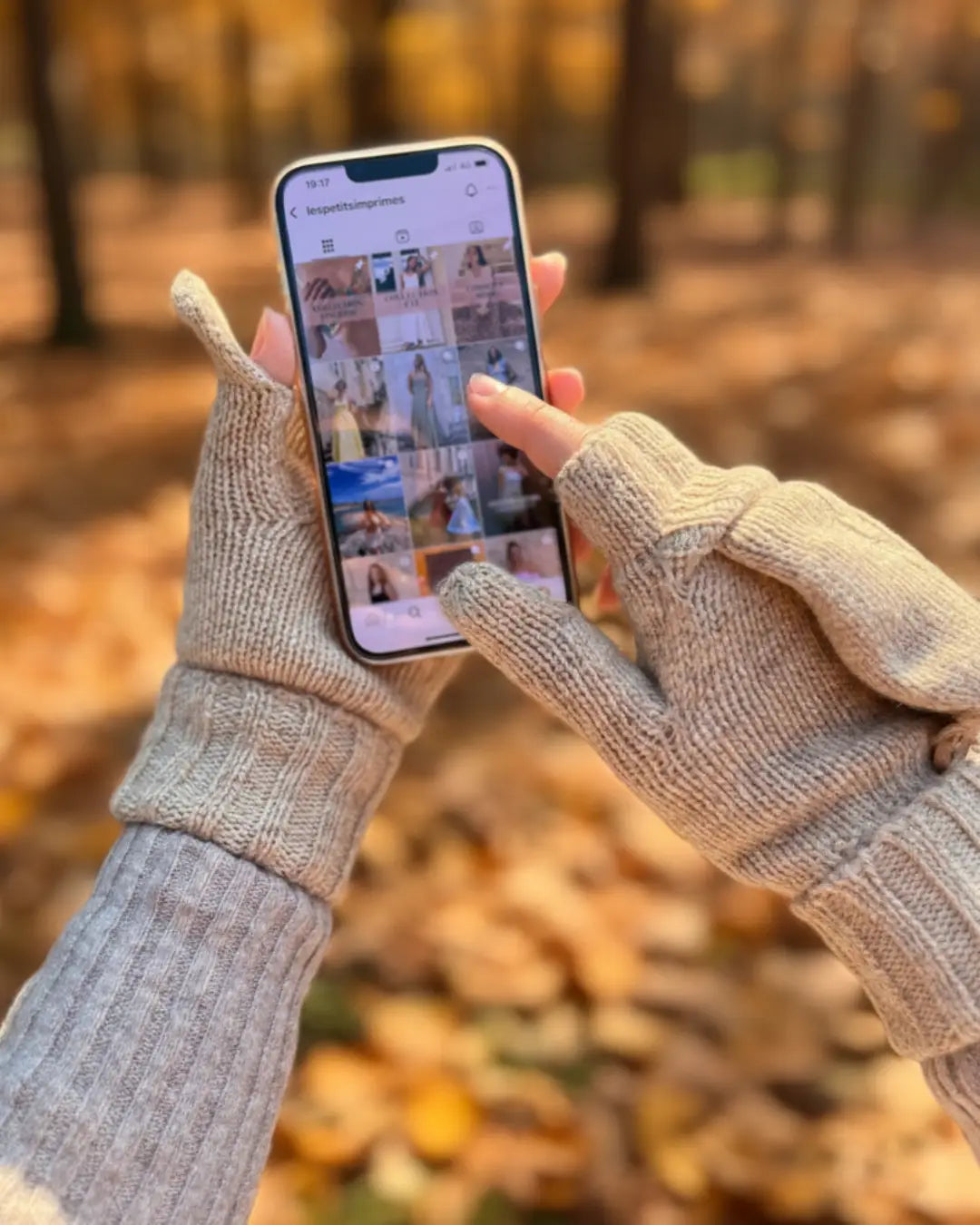Personne portant des moufles mitaines en laine beige utilisant un smartphone en forêt à l'automne.