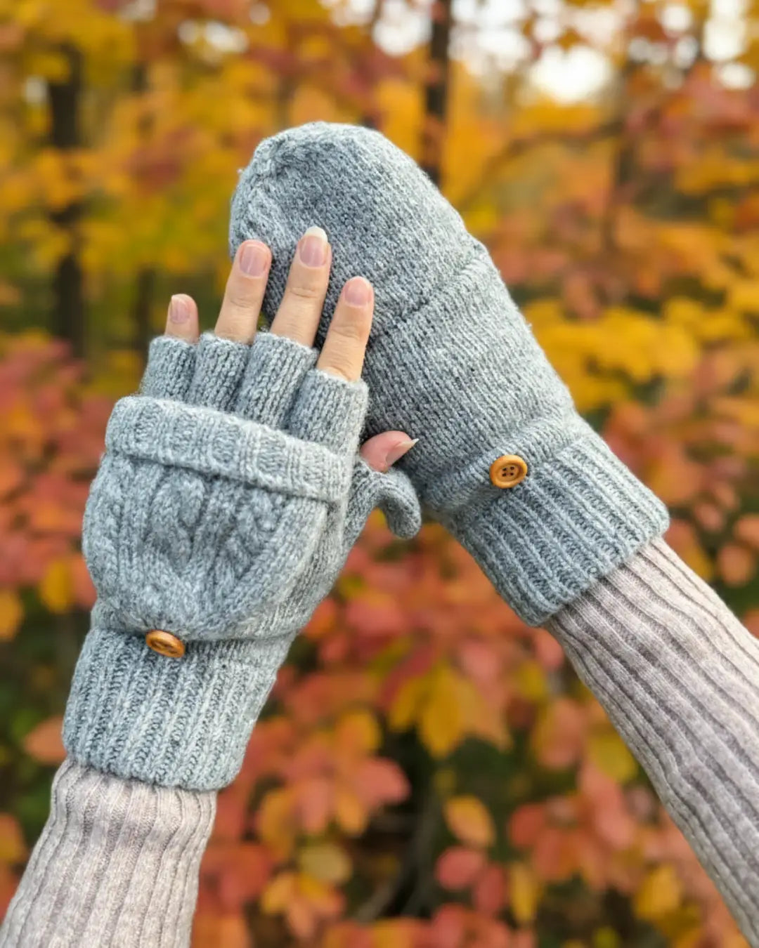 Gants mitaines en laine grise avec boutons en bois sur fond d'automne, idéales pour garder vos mains au chaud.