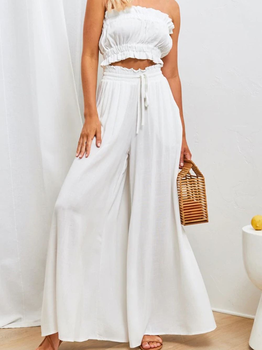 Pantalon large fluide femme pour l'été, couleur blanche, tendance et élégant, porté avec un haut assorti et un sac à main.