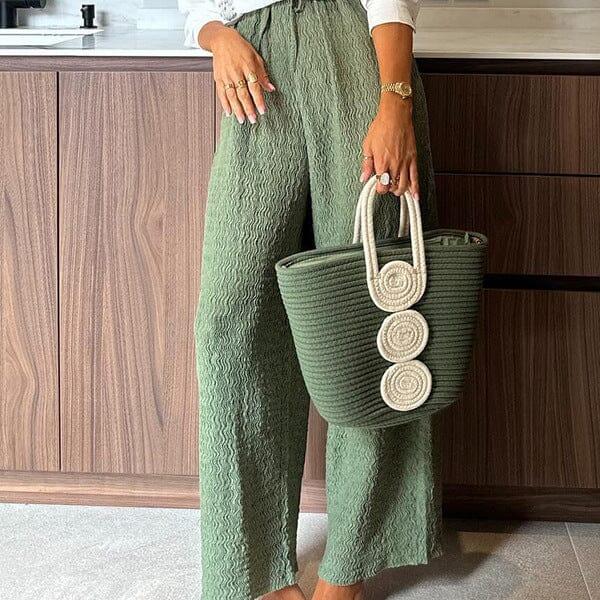 pantalon large et fluide vert tiphaine porté par une femme tenant un sac assorti debout dans une cuisine moderne