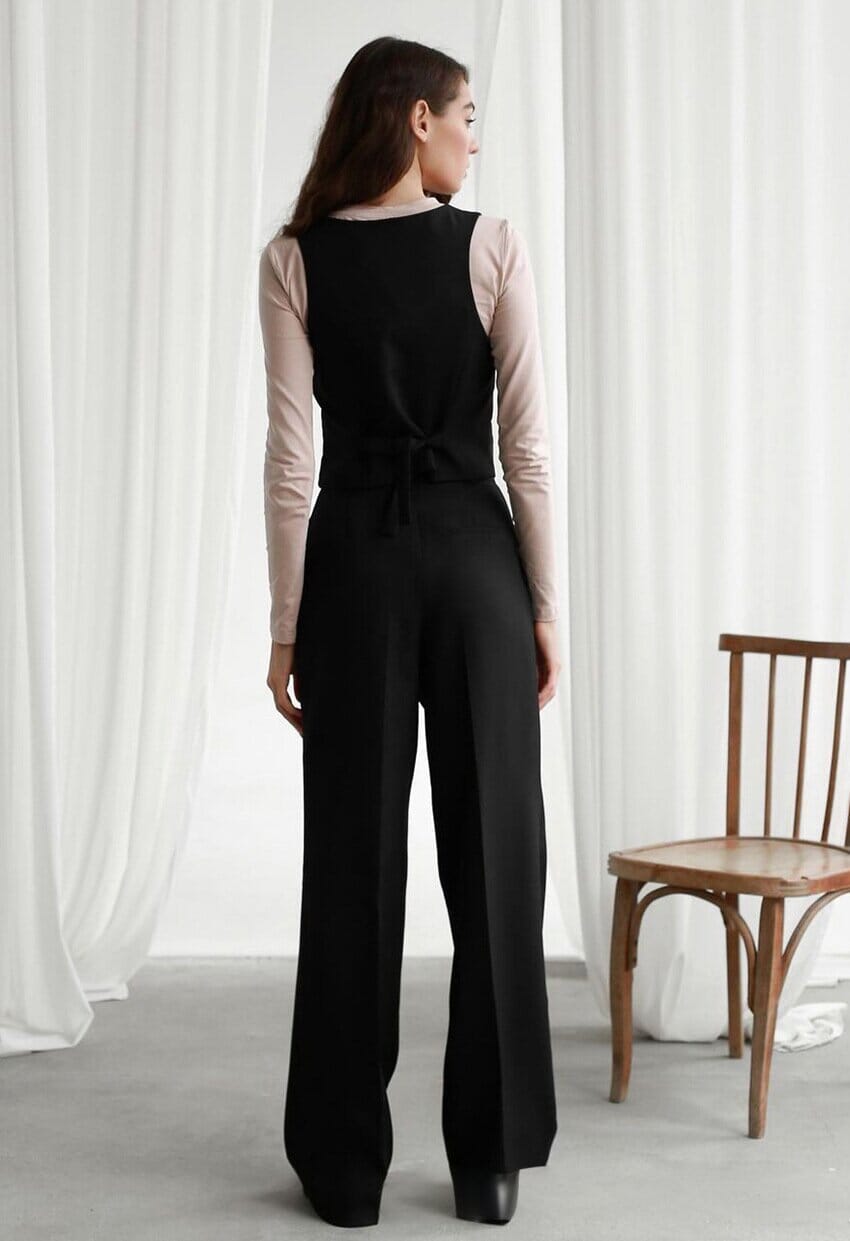 femme portant un pantalon fluide taille haute noir de la marque jane, vue de dos, dans un décor intérieur élégant