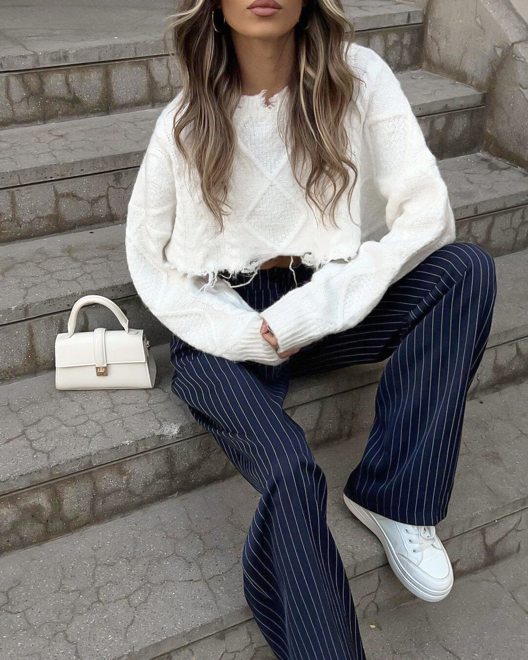 femme assise en escaliers portant un pantalon rayé bleu en combinaison avec un pull blanc et des baskets blanches