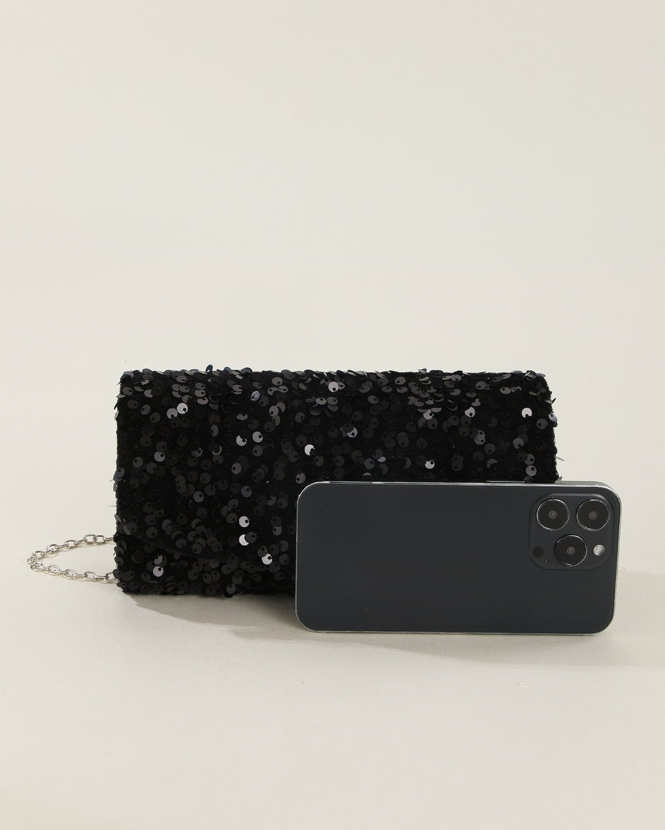 Pochette de soirée noire à sequins Jillian avec chaîne, mise en scène à côté d'un smartphone pour comparaison de taille.