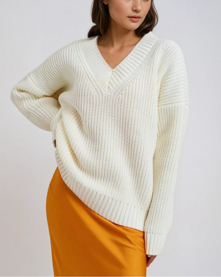 Pull col V manches longues maya en maille blanche, porté avec une élégante jupe orange pour un look chic et moderne.