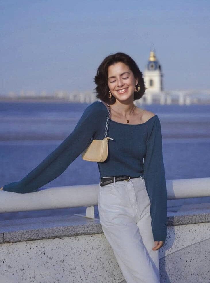 femme souriante portant le pull col carré émilie en bord de mer avec un paysage urbain en arrière-plan