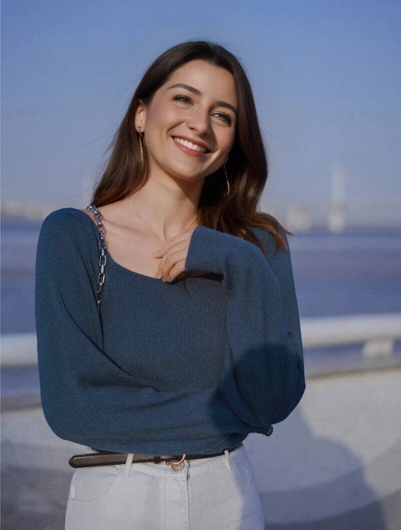 femme souriante portant un pull col carré émilie bleu en maille légère avec une ceinture noire et un fond de paysage flou