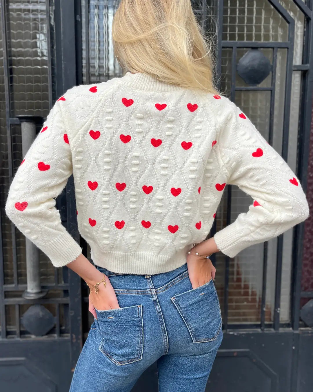 Dos d'une femme portant le pull en laine décoré de cœurs rouges de la collection Nadège avec jean ajusté.