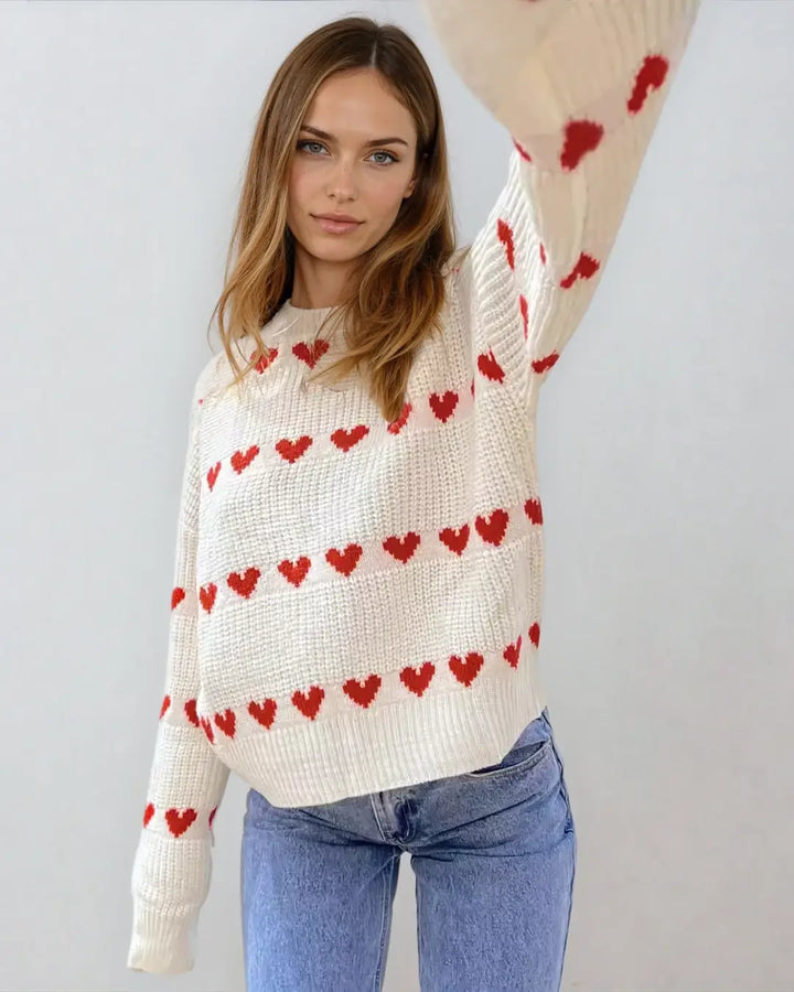 Pull en maille blanc avec des motifs de cœurs rouges porté par une femme vêtue d'un jean, style décontracté et chic.