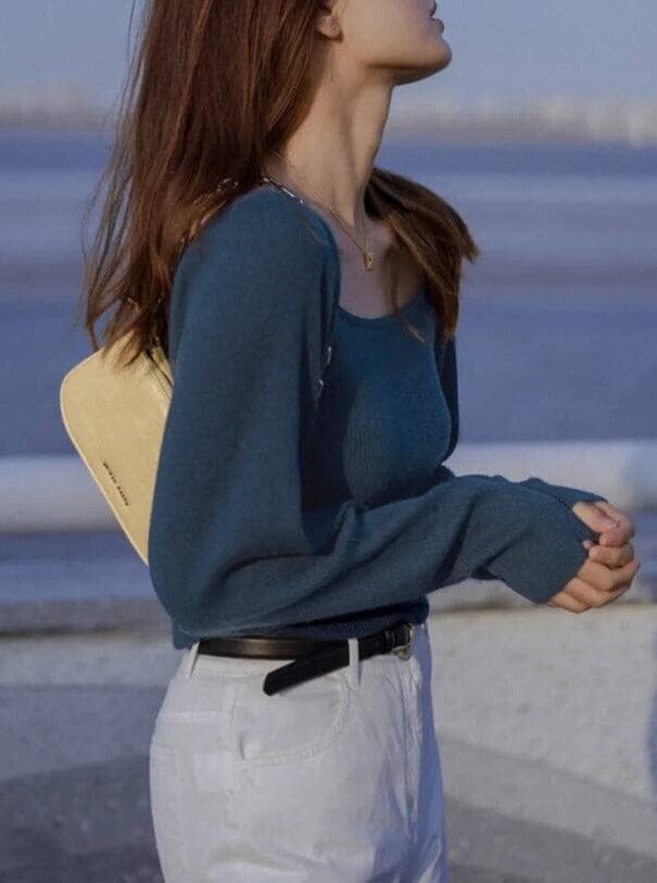 femme portant le pull col carré Émilie de couleur bleue avec pantalon blanc et sac beige en bord de mer