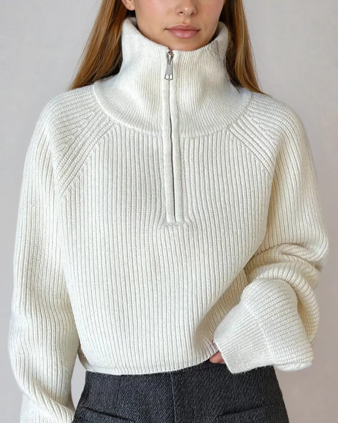 Femme portant un élégant pull à zip court en laine douce, de couleur blanche, avec col haut idéal pour l'hiver.
