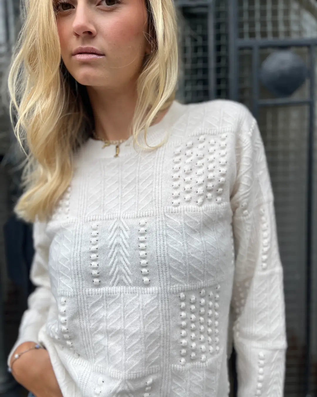 Femme portant un pull en laine blanc avec motifs texturés, idéal pour un look chic et confortable en toute saison.