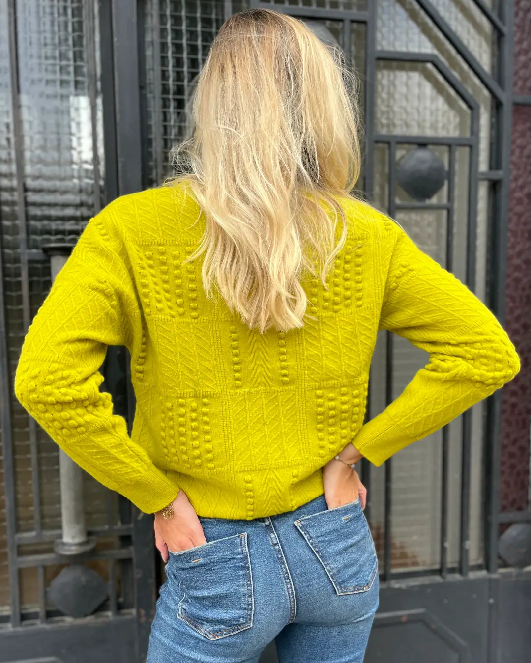 Femme portant un pull en laine jaune vif, en plein air, soulignant son dos, idéal pour l'hiver, mode élégante.