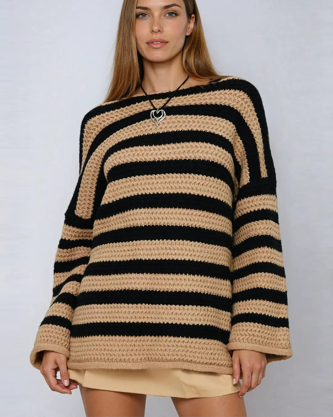 Femme portant un pull oversize rayé noir et beige avec col bateau, design moderne et confortable pour l'hiver.