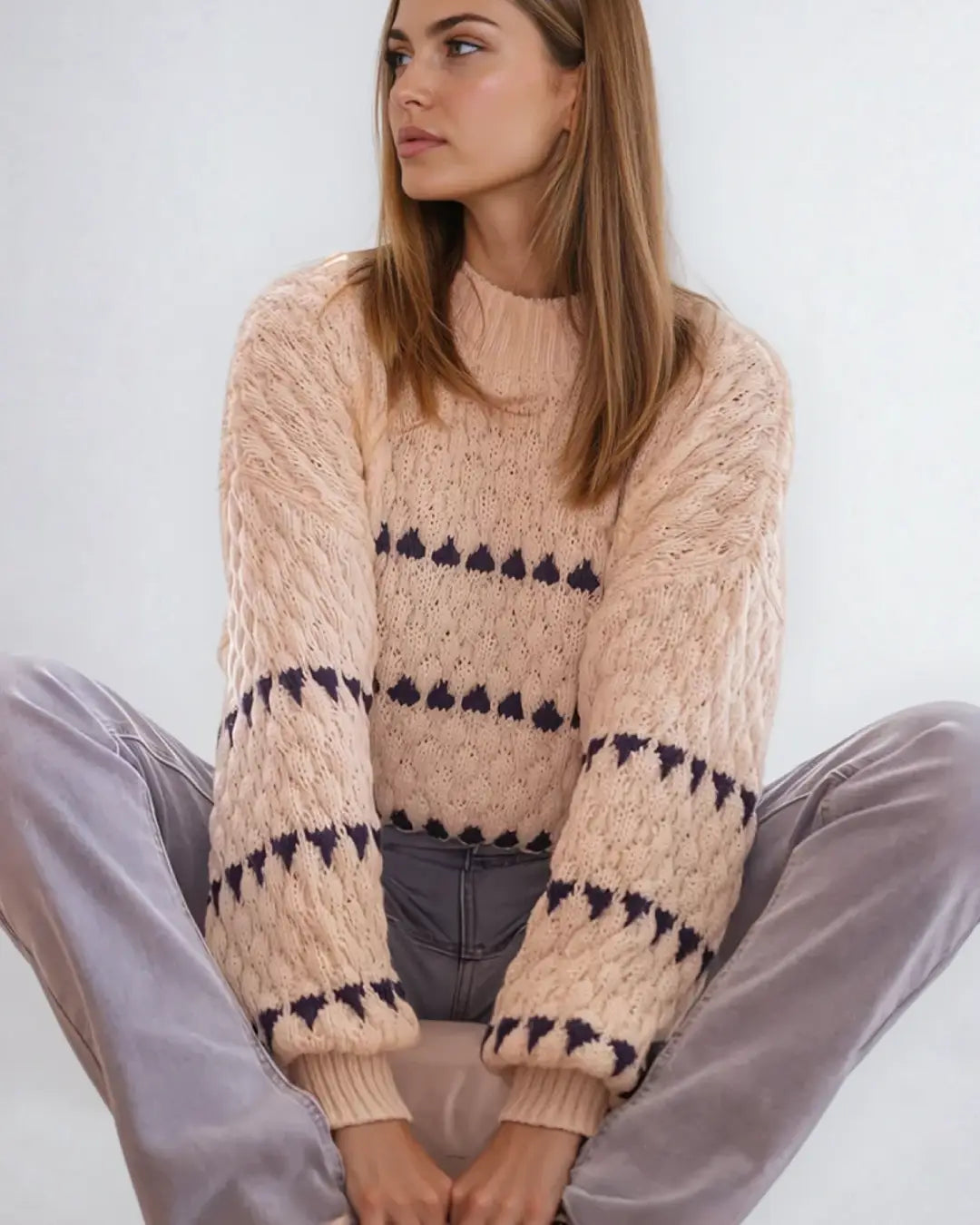 Pull en maille point boule Kira couleur beige avec détails foncés, porté par une femme assise, ambiance décontractée.