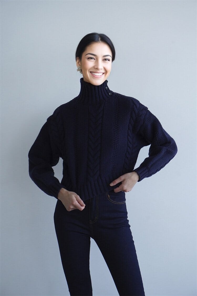 Modèle souriant portant un pull torsadé court bleu marine, idéal pour un look automnal tendance et décontracté.