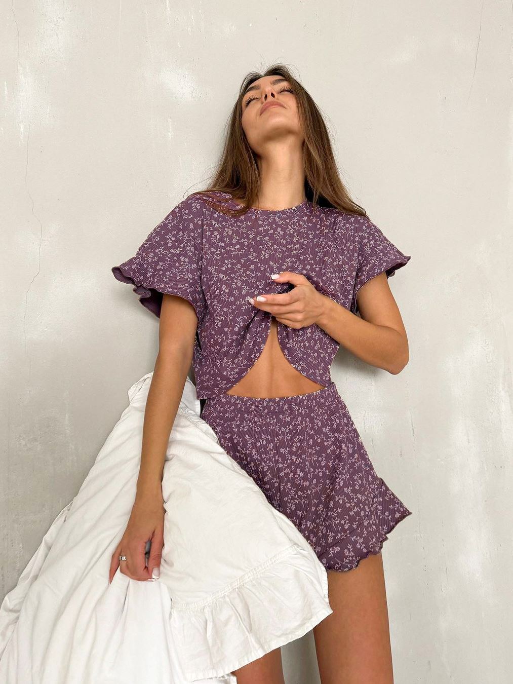 pyjama fleur femme capucine en ensemble violet à motifs floraux avec coupe ovale à la taille, tenu devant un mur blanc