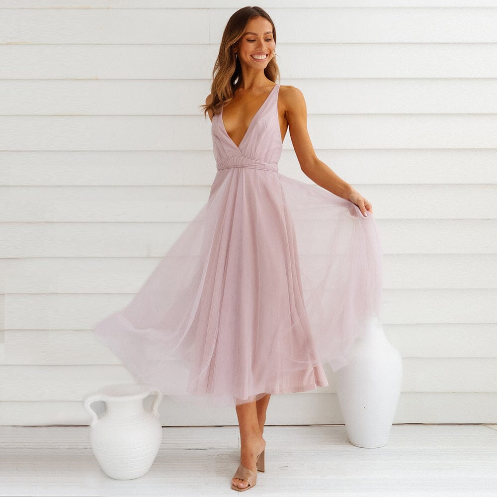 robe longue en tulle rose avec un décolleté plongeant portée par une femme souriante dans un décor blanc minimaliste