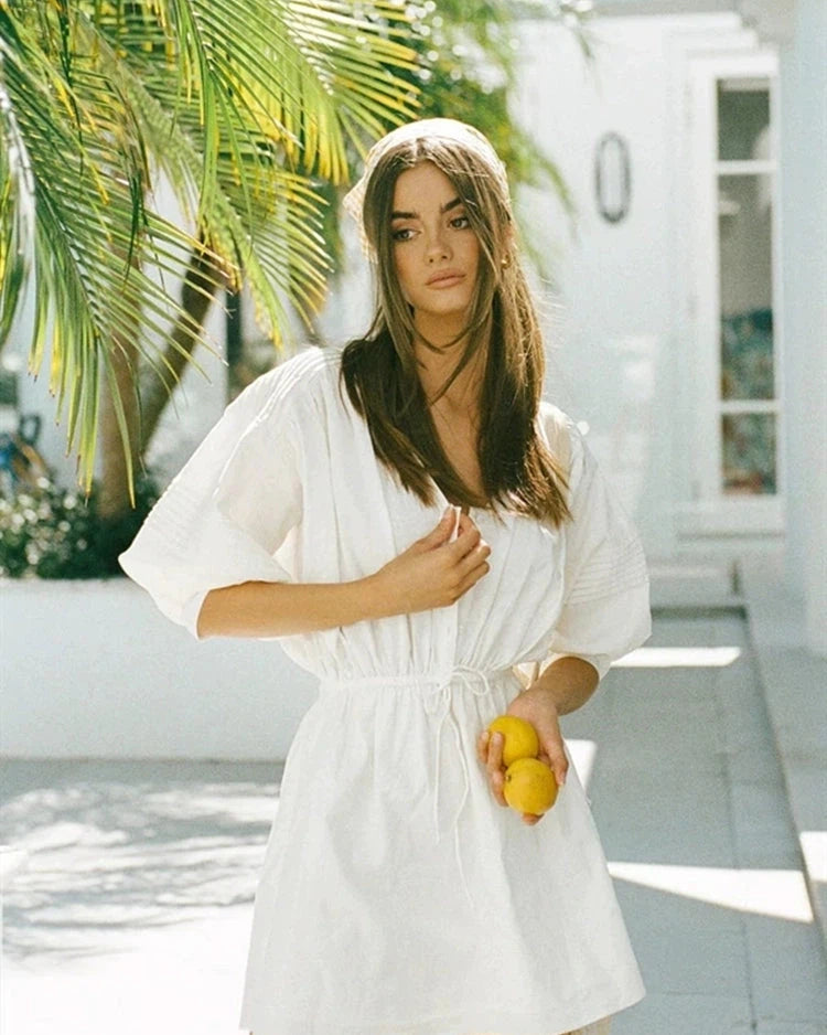 femme portant une robe courte blanche sabine avec des citrons à la main dans un cadre tropical en été