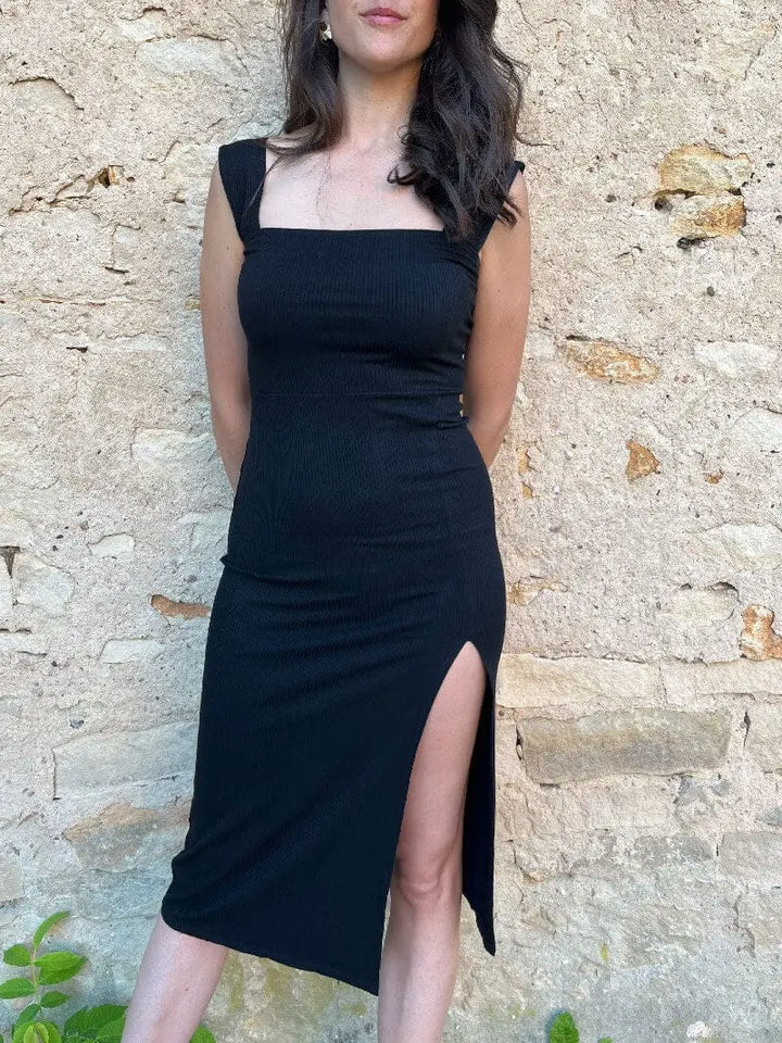 Robe longue moulante Alba en tissu noir avec fente élégante, mise en valeur par un décor minimaliste et moderne.