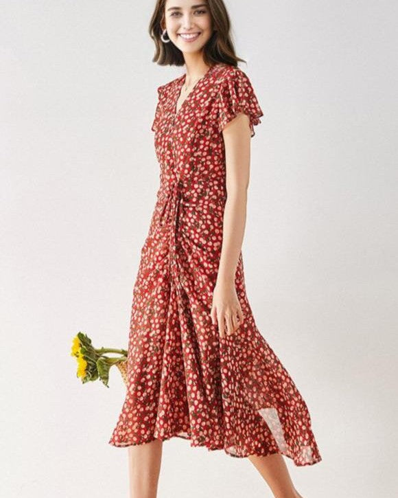 femme souriante portant une robe longue rouge avec motifs floraux, tenant un bouquet de tournesols et posant pour la photo