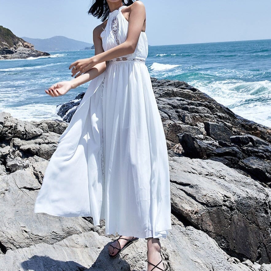 robe longue blanche mathilde en mousseline haute qualité avec dos nu devant l'océan sur une plage rocheuse