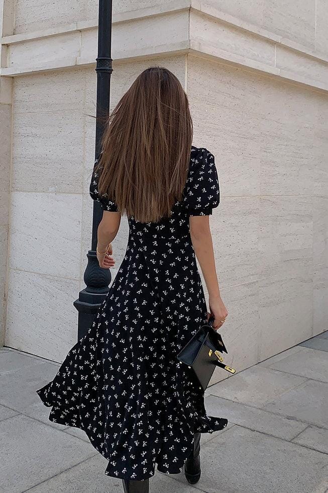 femme de dos portant une robe rétro à nœuds de la marque lison, marchant en extérieur avec un sac à main noir