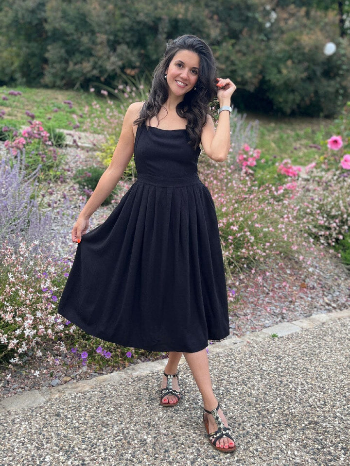 Robe en lin noir au design dos croisé, portée dans un jardin fleuri, mettant en valeur un style estival élégant.