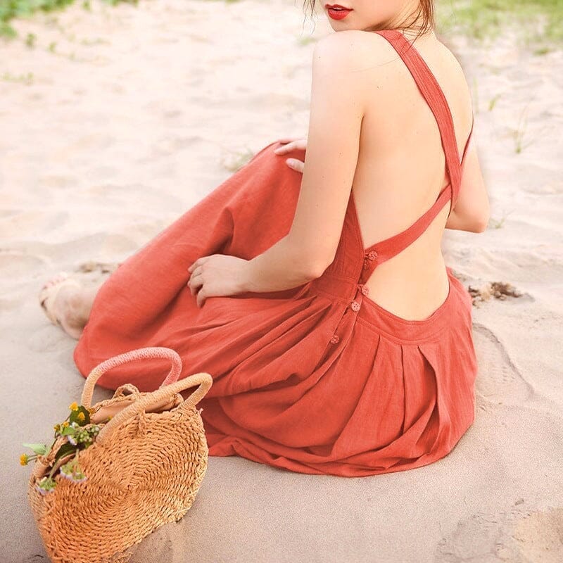 jeune femme portant une robe longue dos nu en lin sur le sable avec un sac en osier à ses côtés