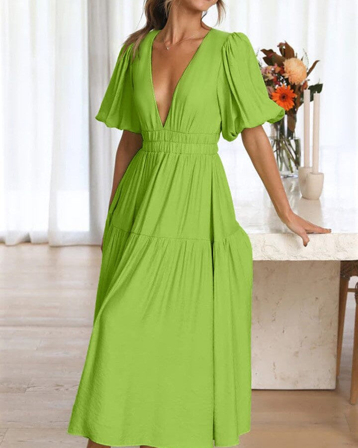 femme souriante portant une robe verte longue avec décolleté plongeant et manches bouffantes dans un intérieur lumineux