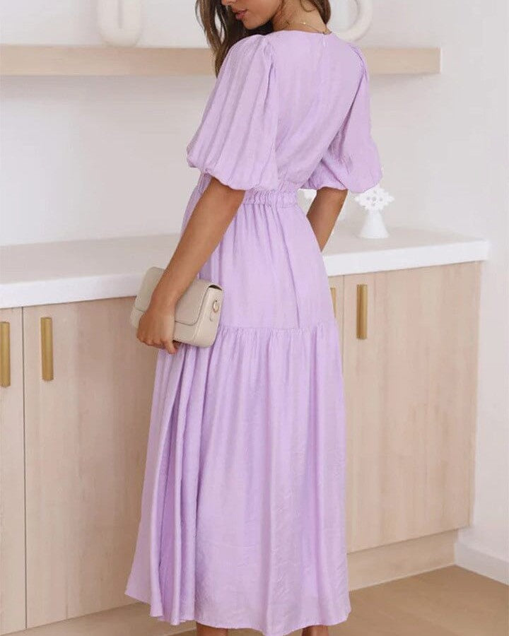 robe décolleté plongeant annie en satin lilas avec manches volantes, femme de dos tenant une pochette beige, déco tamisée