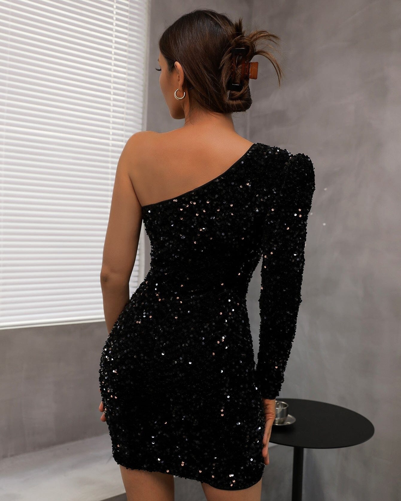 Robe courte asymétrique noire avec paillettes, vue de dos, mettant en valeur les détails brillants et élégants.