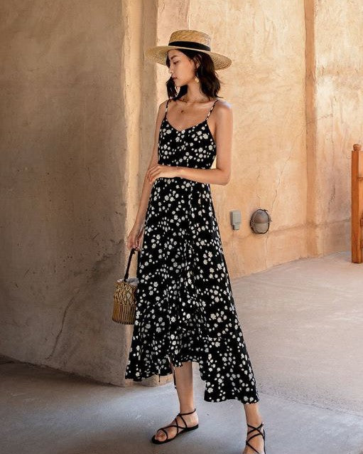 femme portant une robe longue à fleurs noires Aliénor, posant dans un environnement rustique avec un chapeau de paille