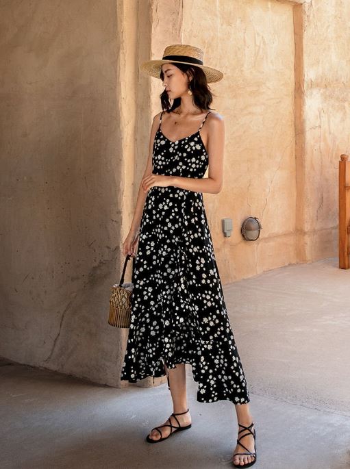 femme portant une robe longue à fleurs noires Aliénor, posant dans un environnement rustique avec un chapeau de paille