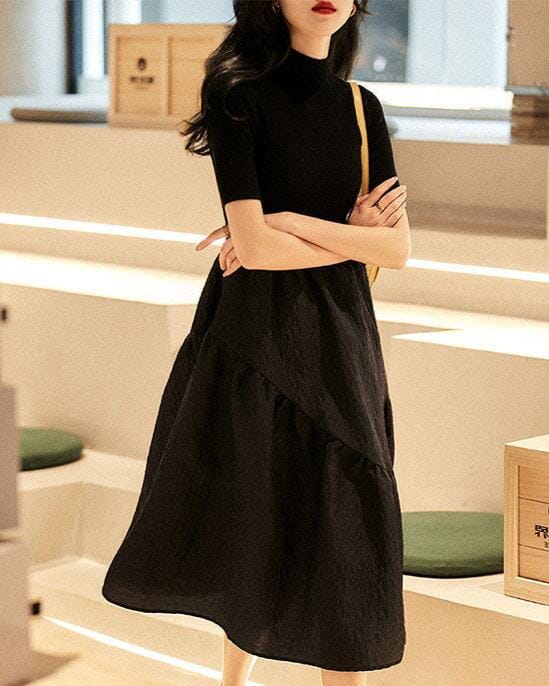 Femme portant une élégante robe noire midi Samara dans un environnement moderne, bras croisés et allure chic.